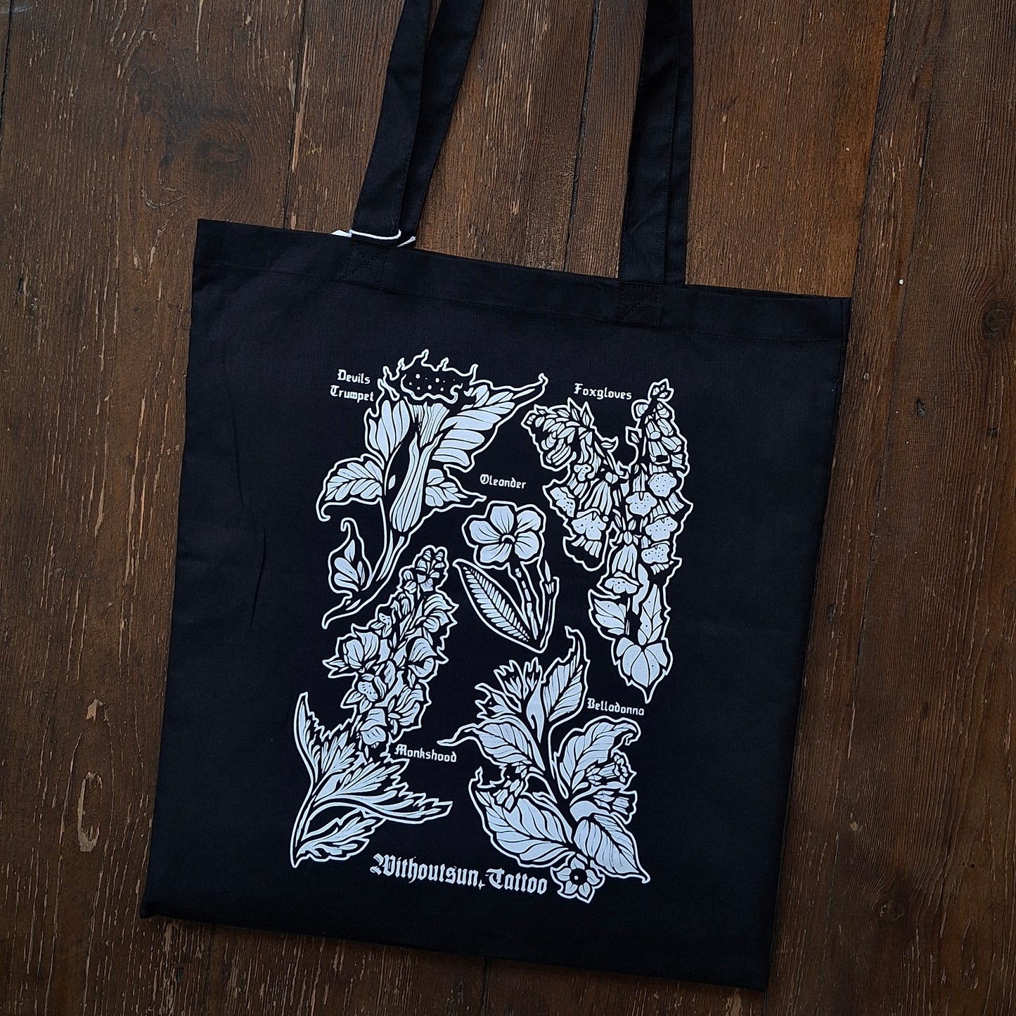 A black canvas tote bag with white poisonous plant illustrations