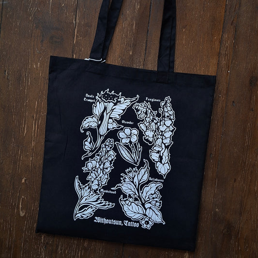 A black canvas tote bag with white poisonous plant illustrations